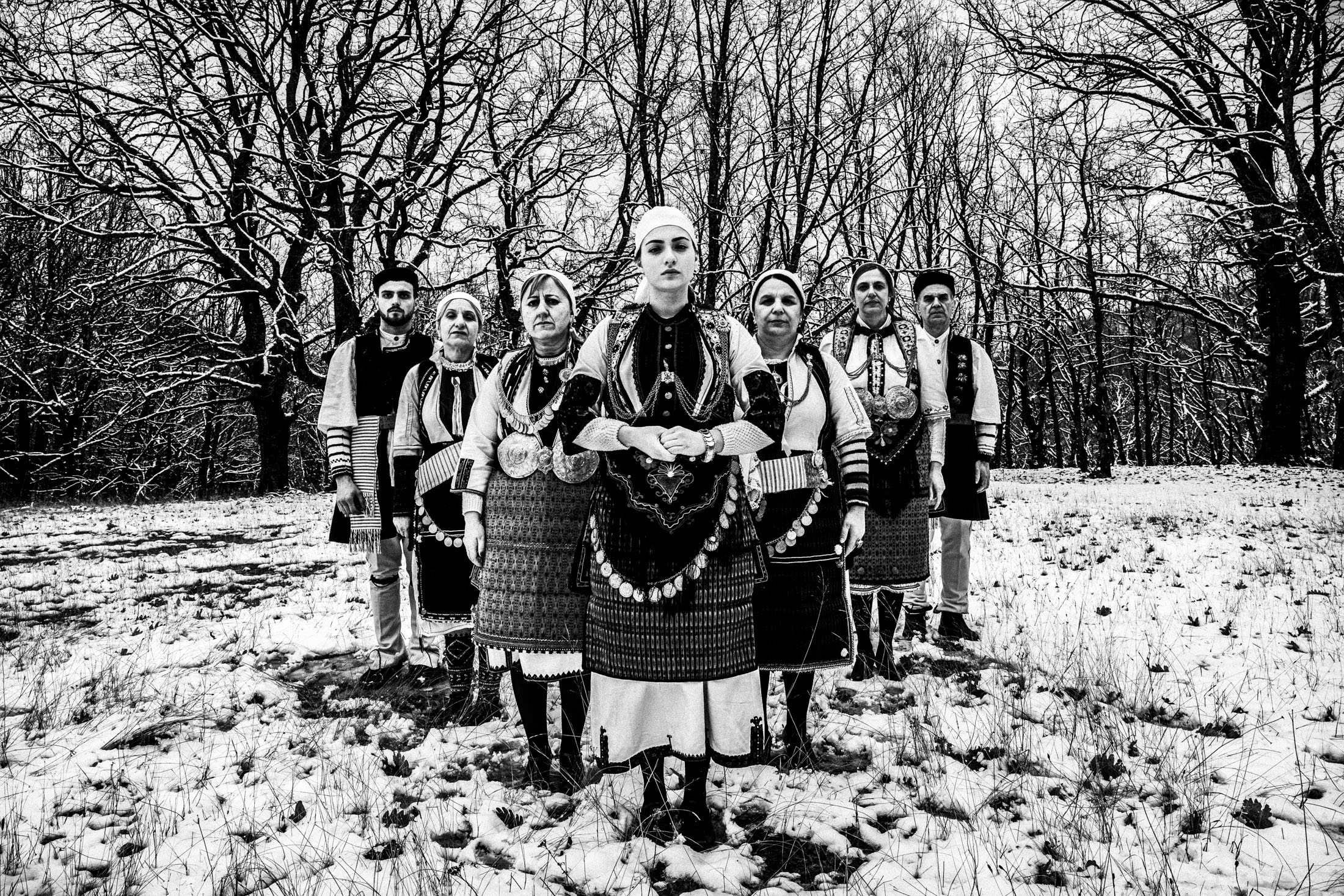 A group of people wearing the local costumes of Kladorachi in Florina, standing in an arrow formation in the snow