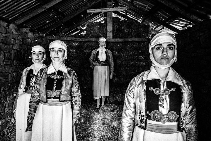 Four women wearing the traditional costumes of Pogoni, Epirus, standing inside a barn in the village of Palaeopyrgos