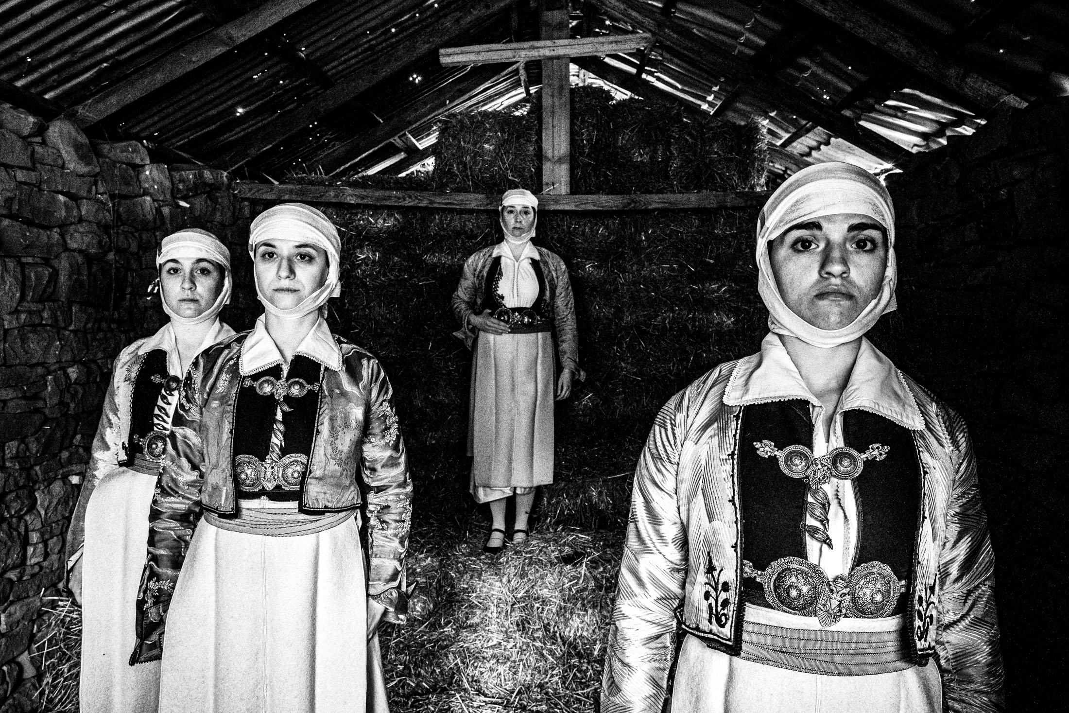 Four women wearing the traditional costumes of Pogoni, Epirus, standing inside a barn in the village of Palaeopyrgos