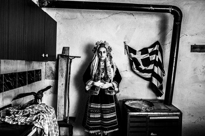 A young woman wearing the local costume of Vryssi in Evros, standing inside the kitchen of a local house.