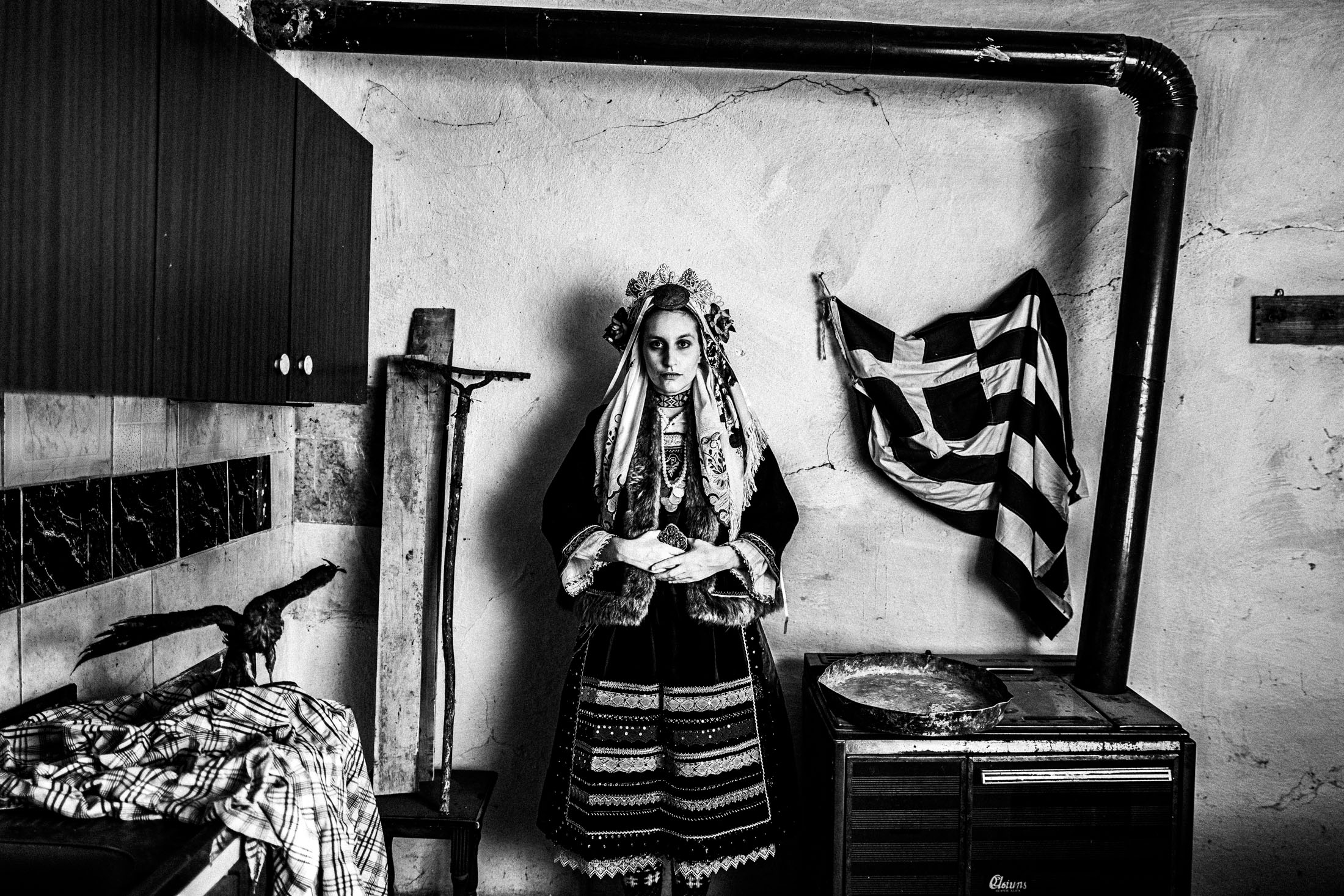 A young woman wearing the local costume of Vryssi in Evros, standing inside the kitchen of a local house.