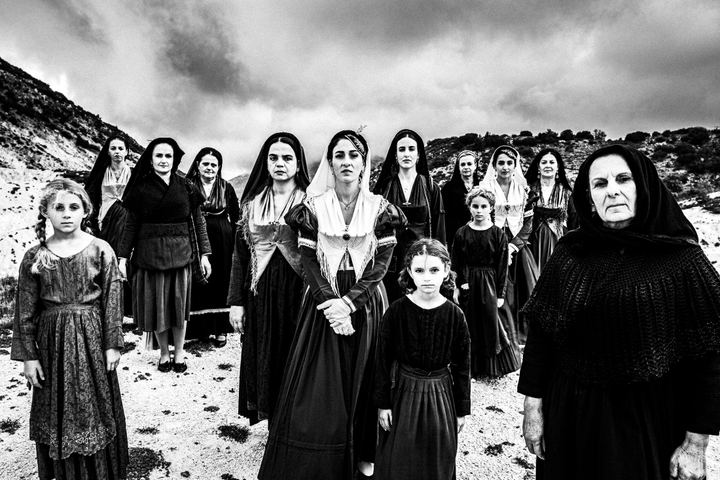 A group of women wearing the costumes of Lefkada standing on a hill with white sand