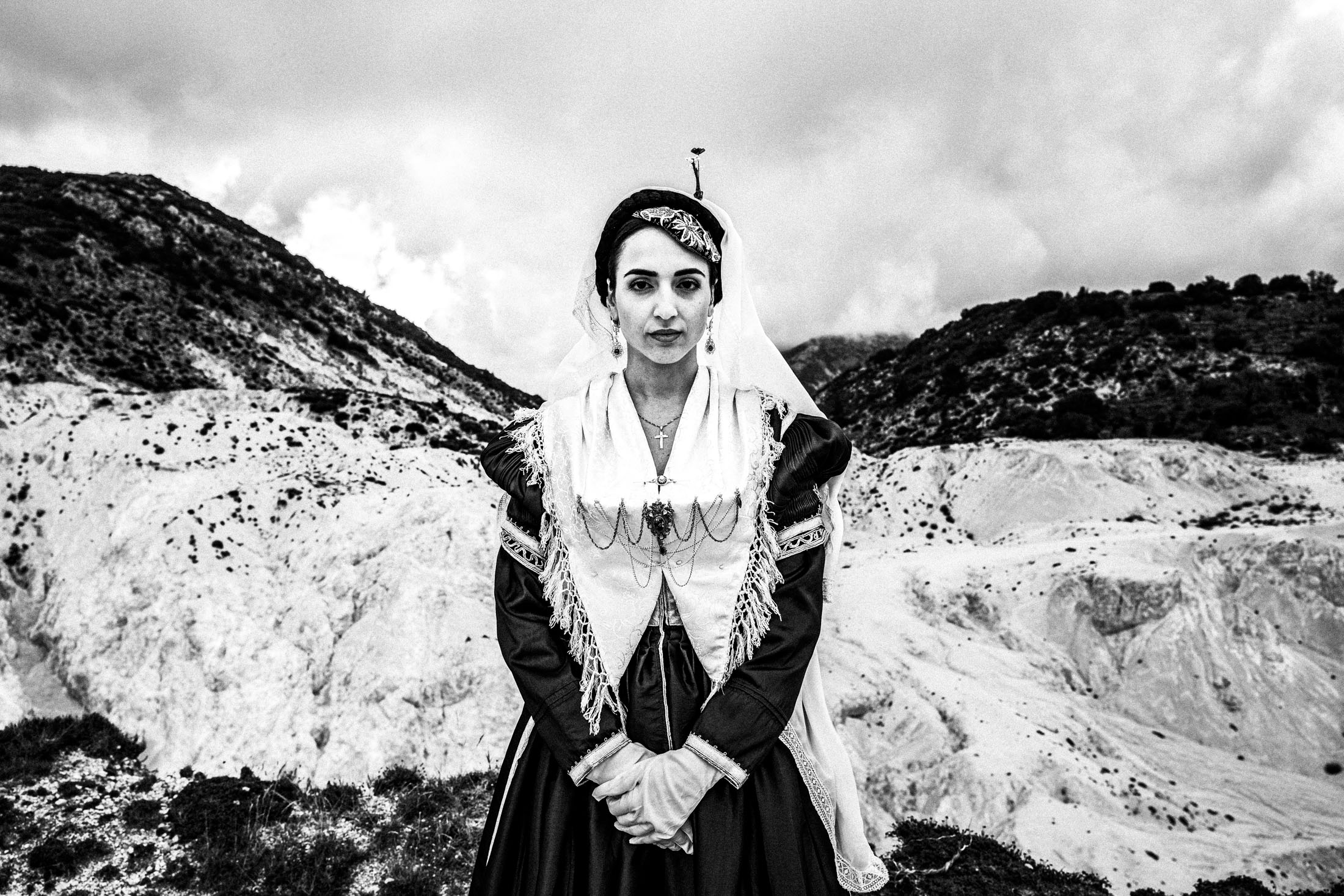 A woman in the bridal dress of Lefkada standing before local mountains with white cliffs
