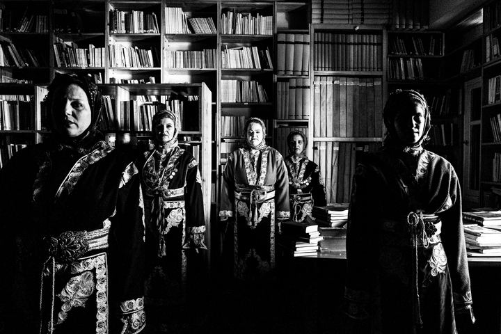 Five women standing in formation, wearing the costumes of Cappadocia, inside the library of Faros Varvassiou on the island of Chios