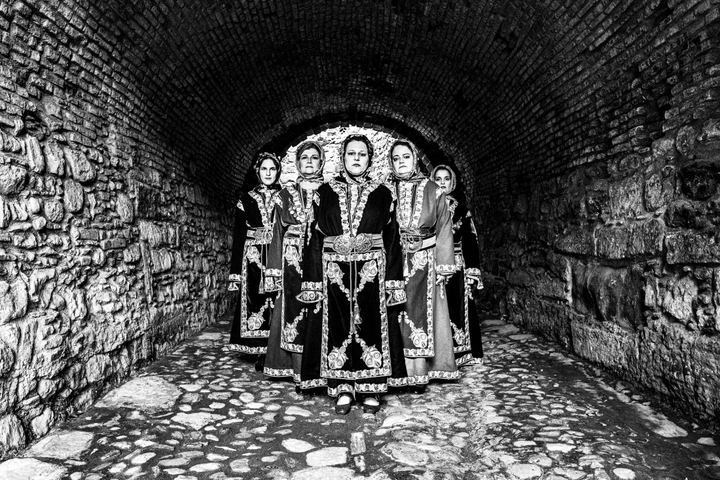 Five women in the traditional dresses of Cappadocia, standing in formation in a stone castle entrance in the city of Chios