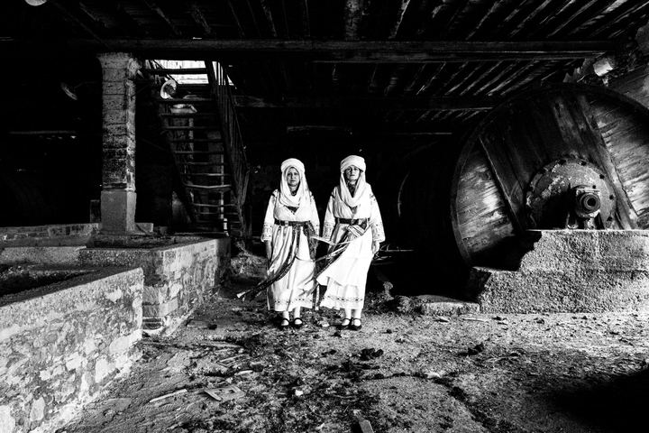 The women wearing the local costumes of Kallamoti in Chios, standing side by side inside an abandoned tannery in the city of Chios