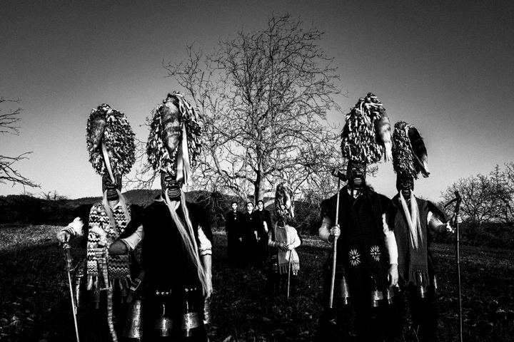 A group of bell-bearers from Sohos carnival and women wearing the local traditional costumes stand by a tree at a local field