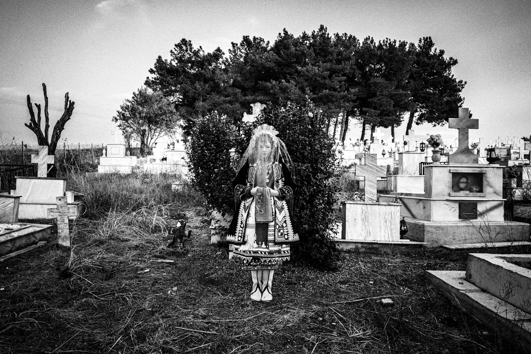 A young woman wearing the local bridal dress of Isaakio, Evros, standing at the local cemetery