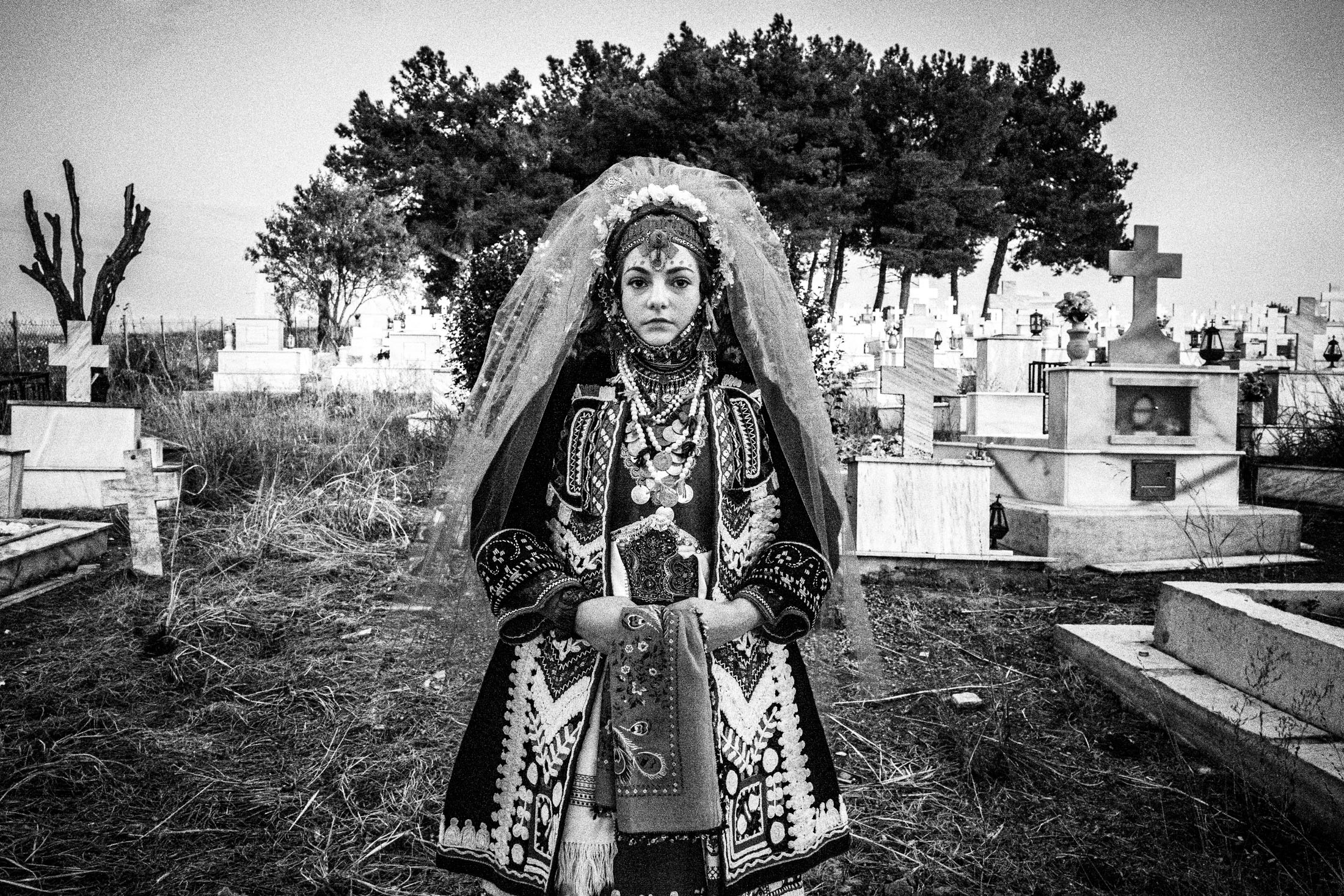 A young woman wearing the local bridal dress of Isaakio, Evros, standing at the local cemetery