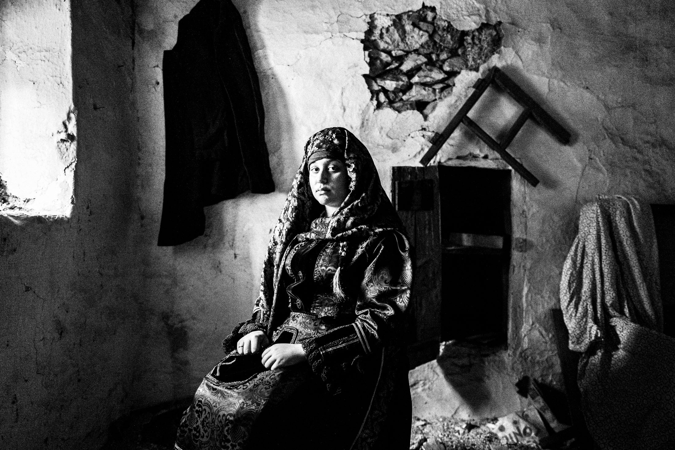 A woman, sitting by a window, in an old abandoned local house, wearing the traditional costume of Kardamyla