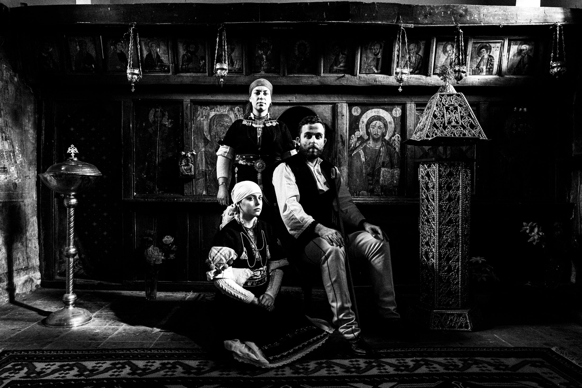 A family of three, wearing the local costumes of Prespes in Florina, posing for a family portrait inside a local orthodox church.