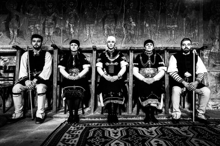 Five persons wearing the local costumes of Prespes in Florina, sitting inside a local orthodox church