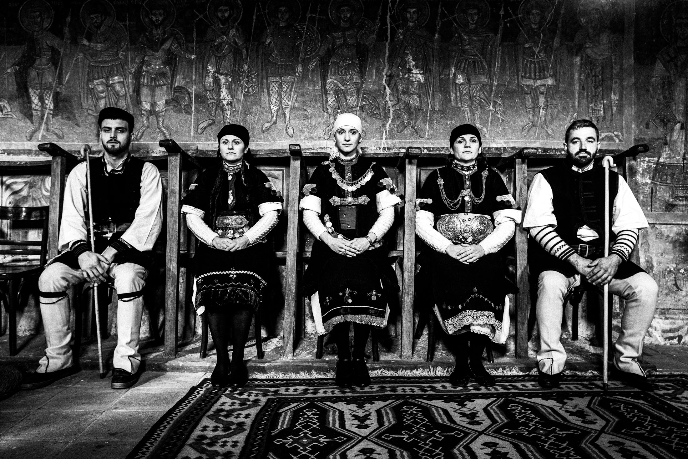 Five persons wearing the local costumes of Prespes in Florina, sitting inside a local orthodox church