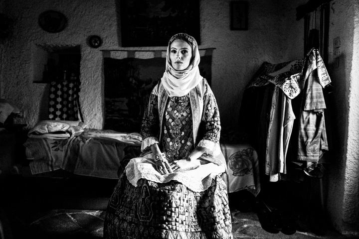 A woman sitting, wearing the local costume of Kalyvia in Attica, inside a local home.