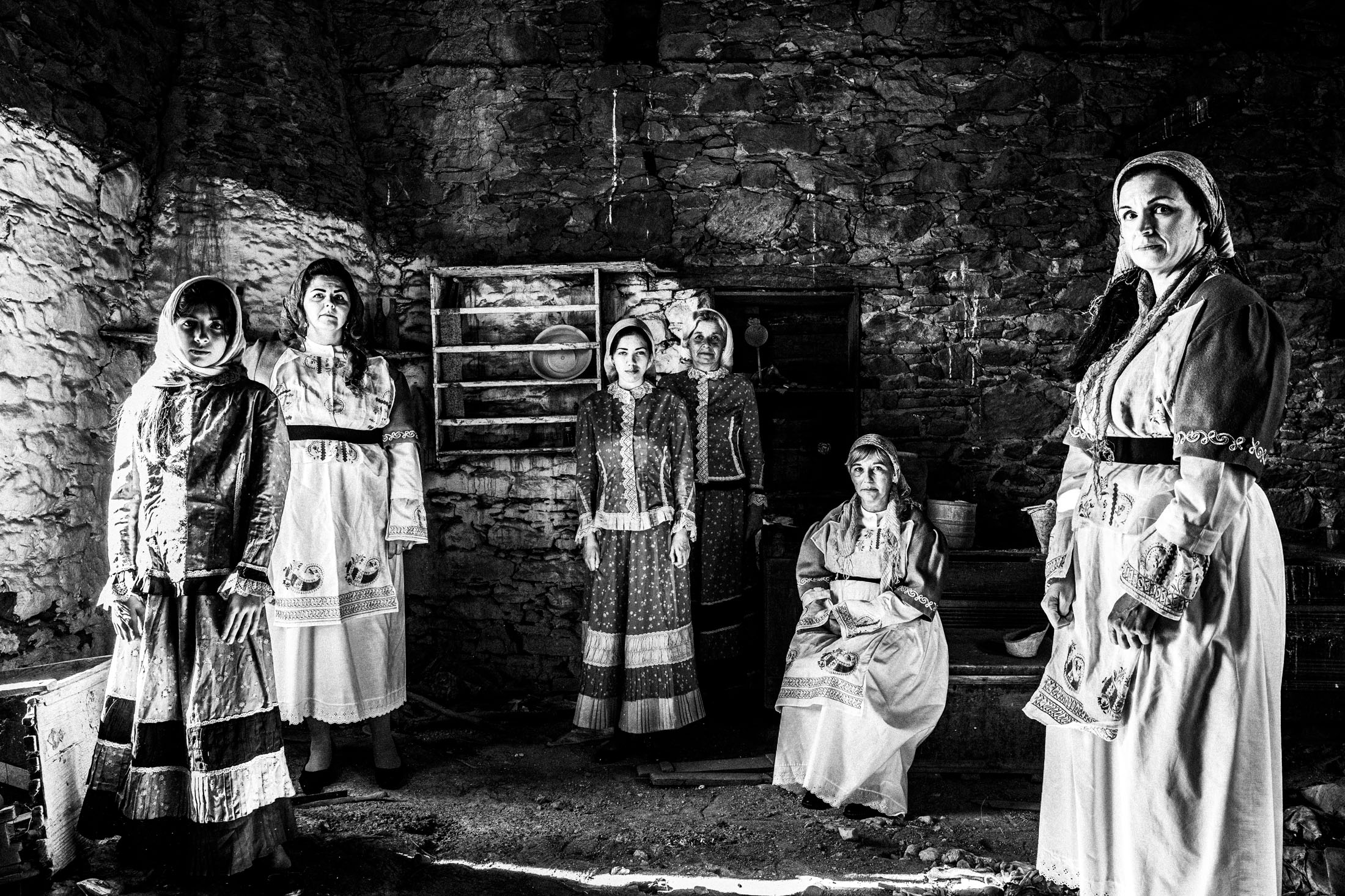 Five women inside the kitchen of an old abandoned local house, wearing the traditional costumes of Volissos, Chios