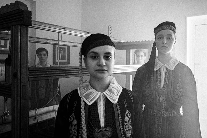 Women wearing the urban dresses of Ioannina Epirus, standing inside a local mansion, around the loom
