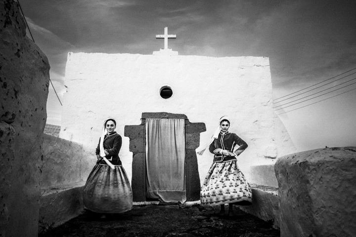 Two young women outside a white washed church, wearing the local costumes of Patmos