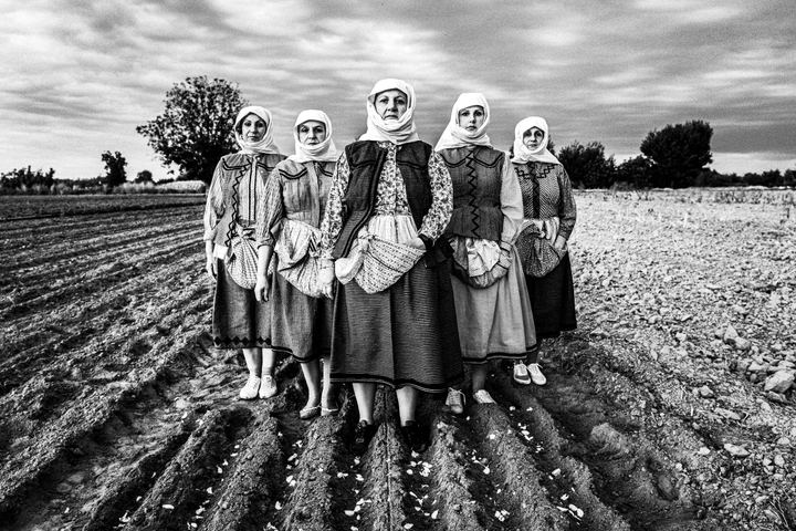Women wearing the local costumes of Nea Vyssa in Evros standing in a freshly ploughed garlic field.