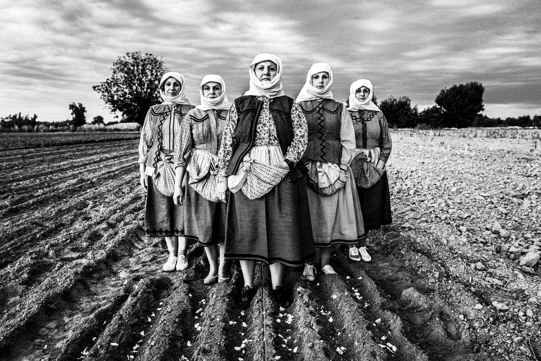 Women wearing the local costumes of Nea Vyssa in Evros standing in a freshly ploughed garlic field.