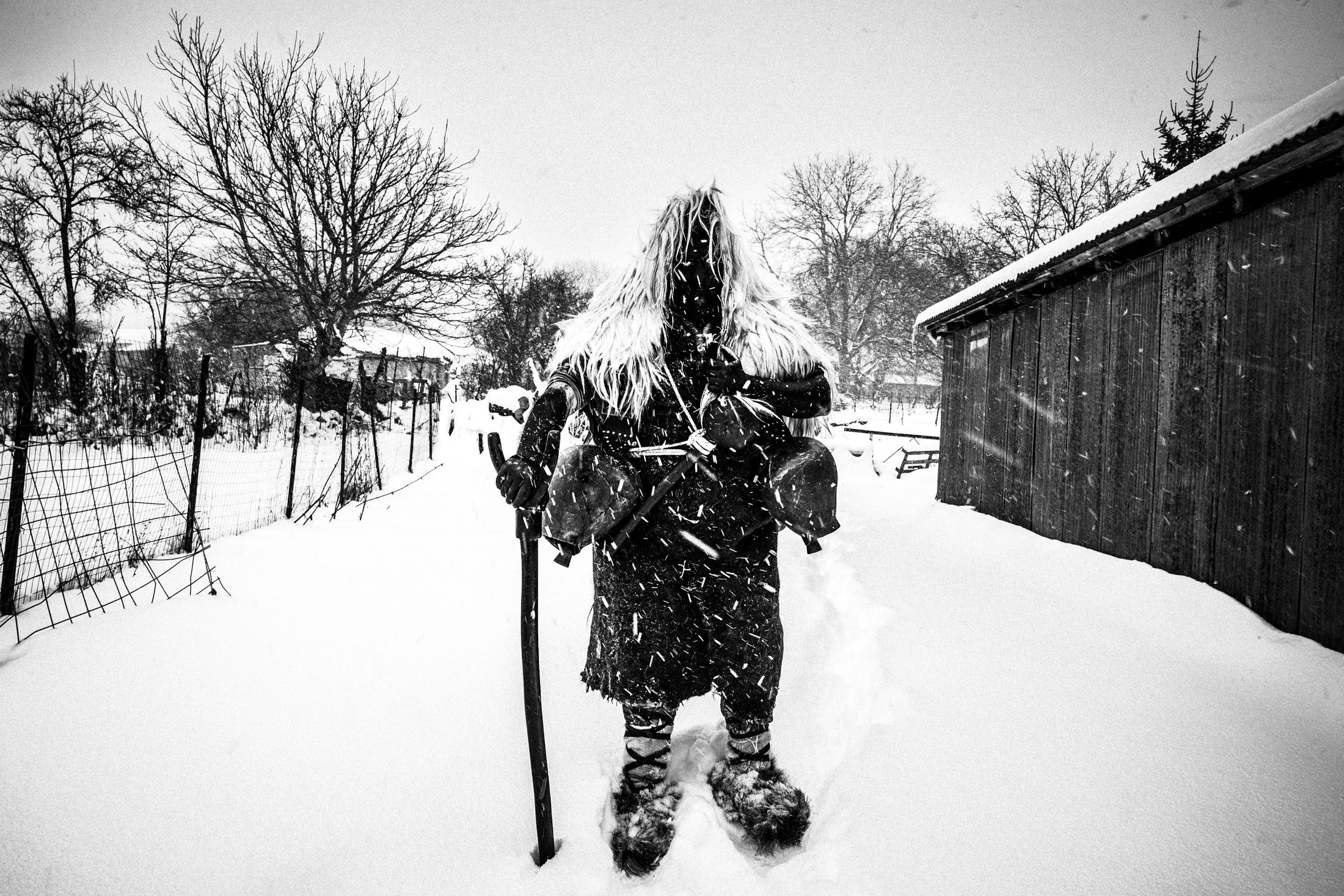A bell-bearer during the custom of Arapides standing in front of a building in the snow at Volakas, Drama.
