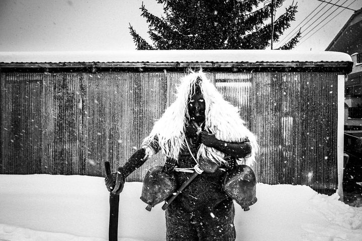 A bell-bearer during the custom of Arapides standing in front of a building in the snow at Volakas, Drama.