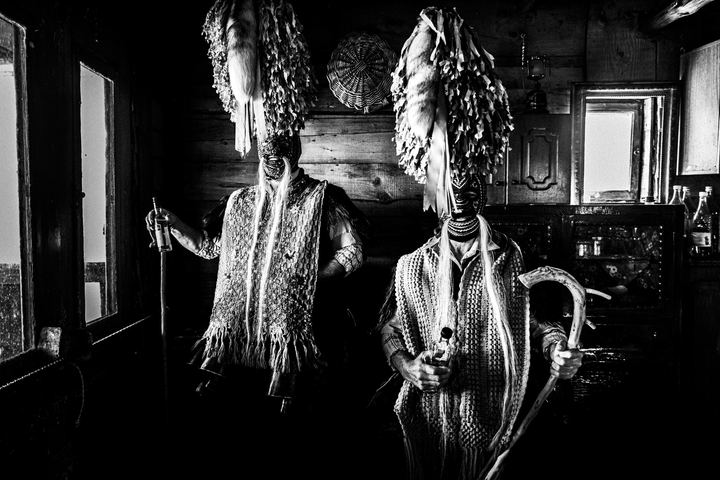 Two masked Koudounoforoi of Sohos wearing tall ribboned headpieces and holding wooden staffs.