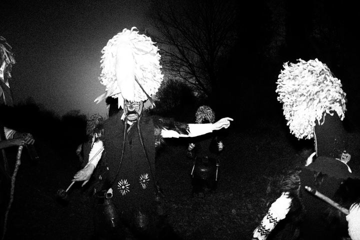 Masked bell bearers of Sohos dancing outdoors at night.