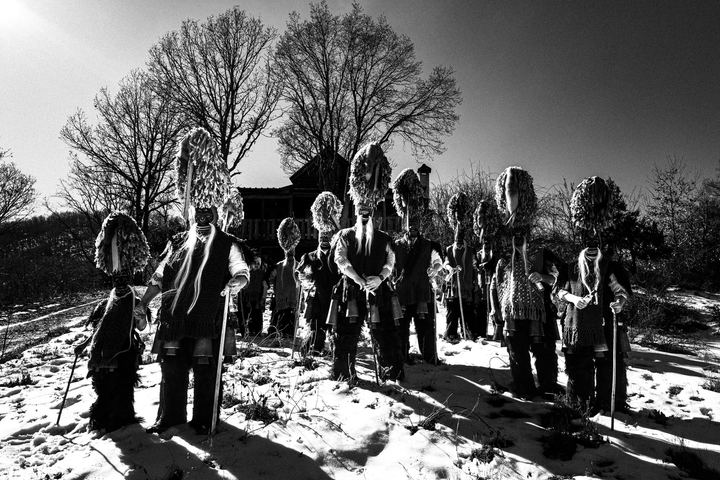 Large group of Koudounoforoi standing in snow near a mountain shelter.