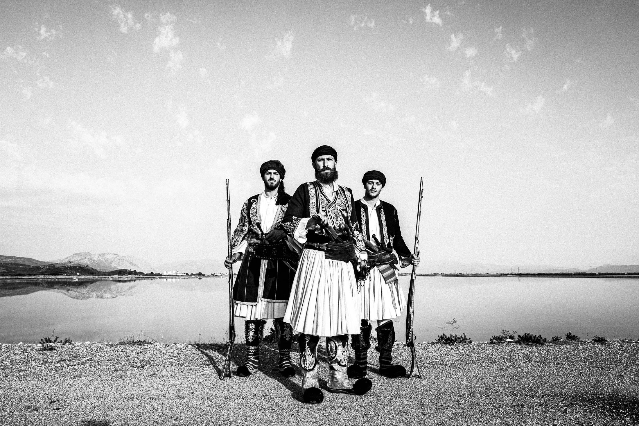 Three armed men in traditional Ntoulamas costume standing beside the lagoon.