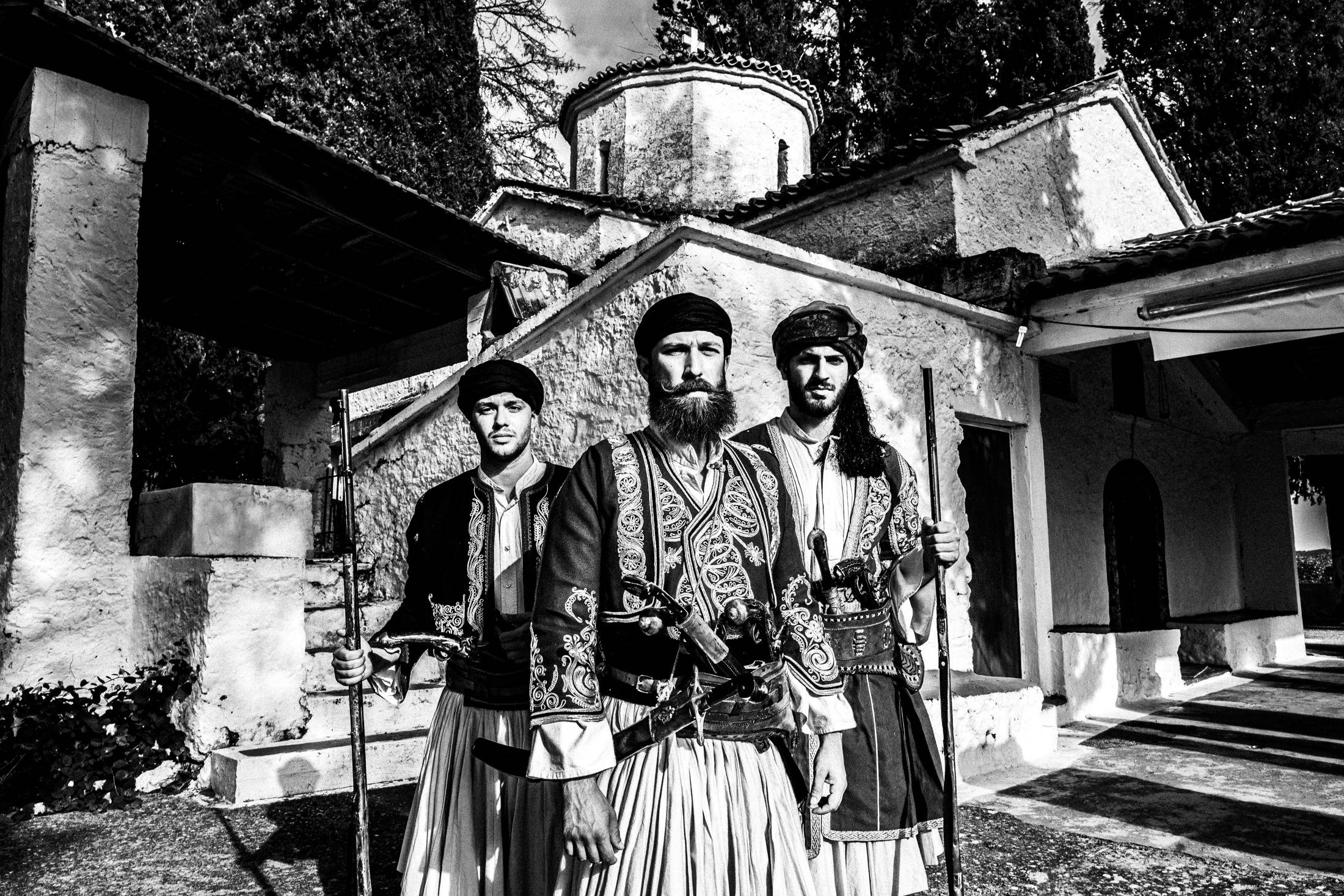 Three men in traditional armed costume standing in front of Saint Simeon church.
