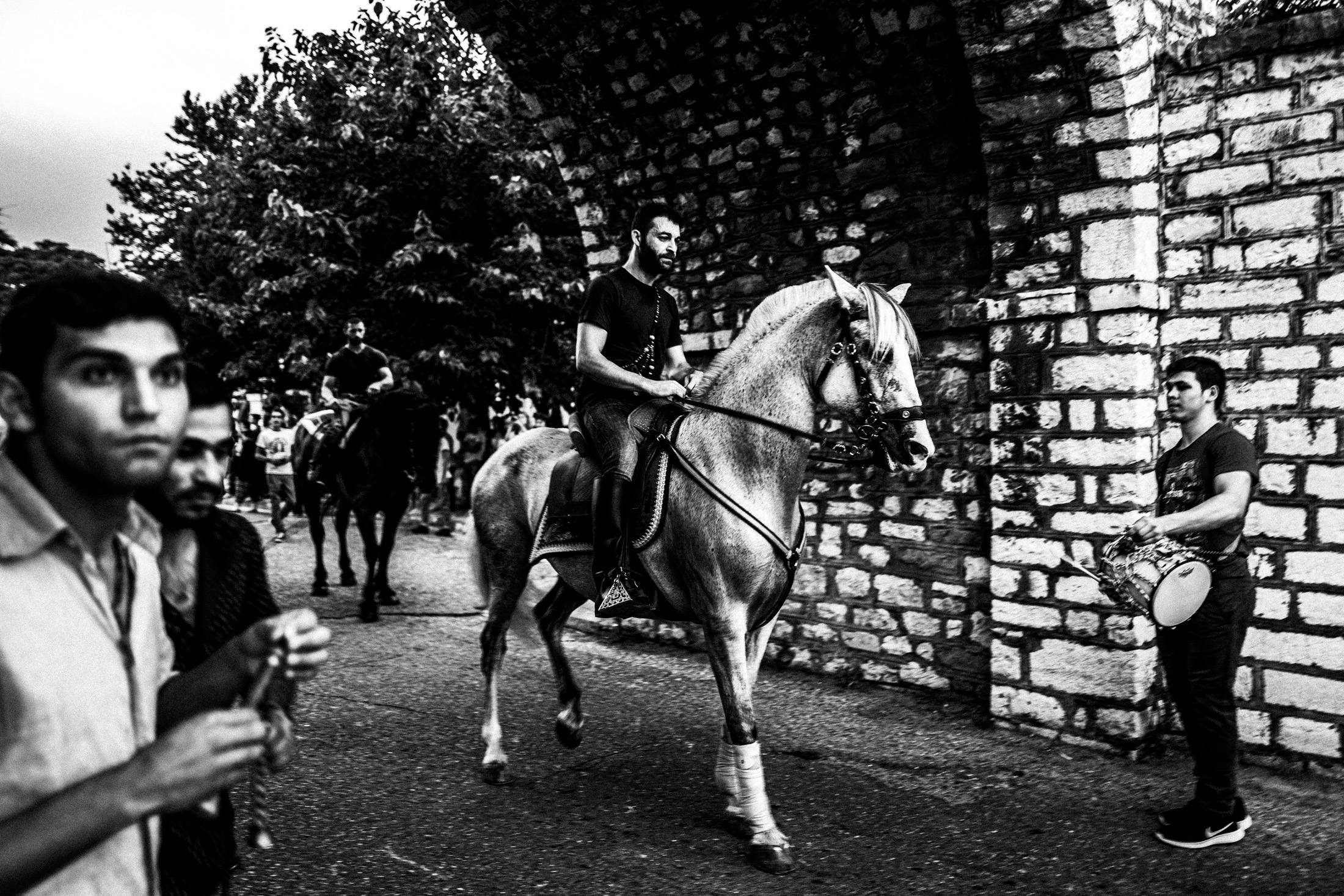 A rider on a white horse passing musicians and spectators during the procession.