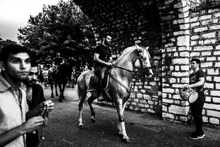 A rider on a white horse passing musicians and spectators during the procession.