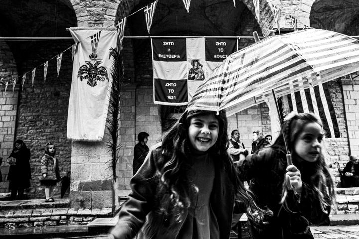 Two smiling children carrying umbrellas in front of Agia Lavra monastery.