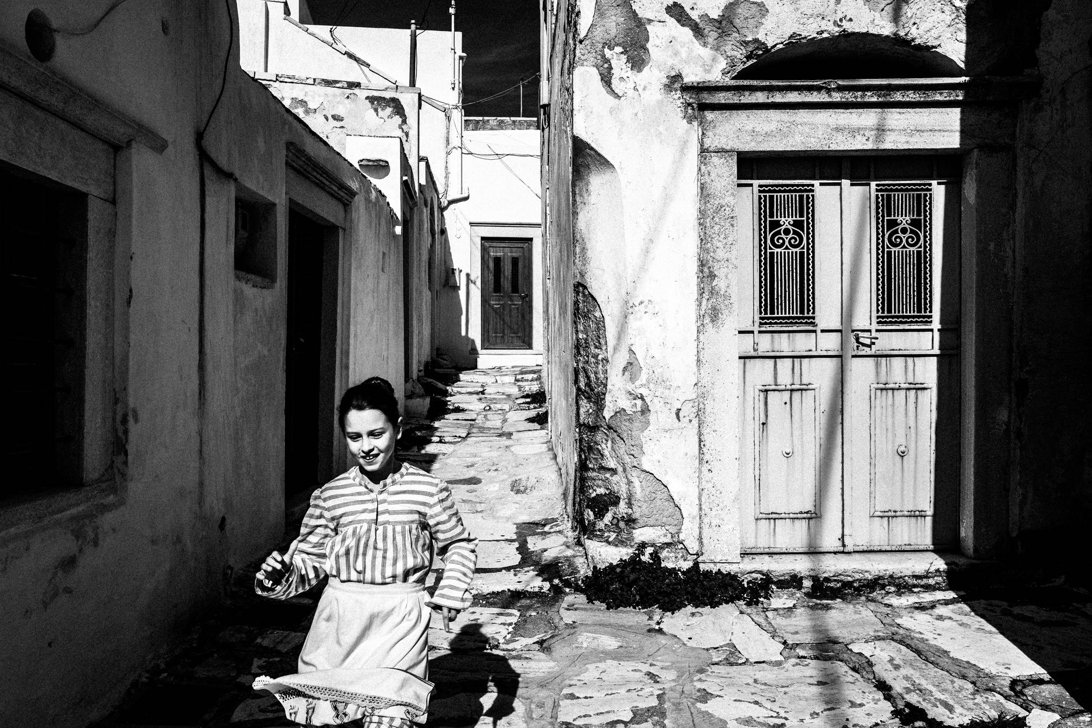 A young girl running through a stone alley in Apeiranthos.