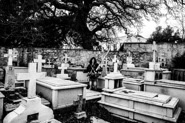 A bell bearer standing among graves at the cemetery of Apeiranthos.