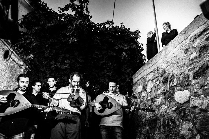 Musicians and villagers moving together through a street in Spili.