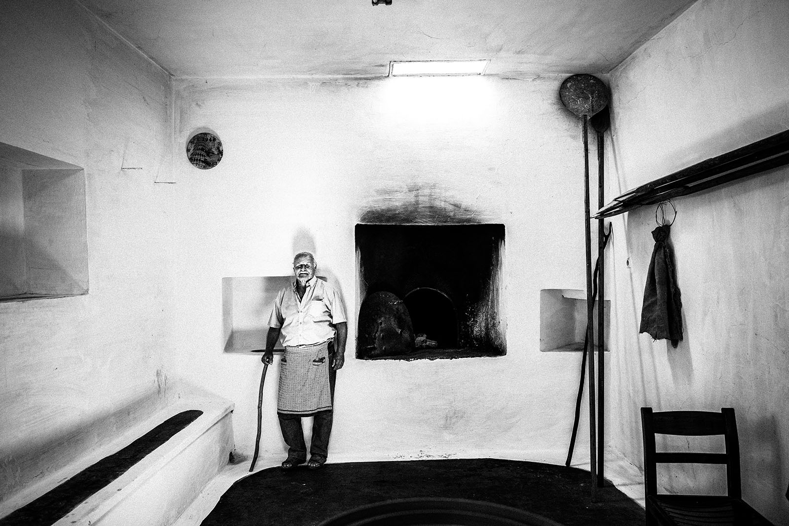 A man standing by the wood-burning oven at Agia Paraskevi monastery in Amorgos