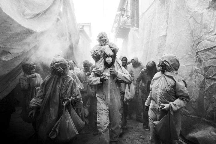 Participants walking through a flour-filled street in Galaxidi, with buildings covered for protection.