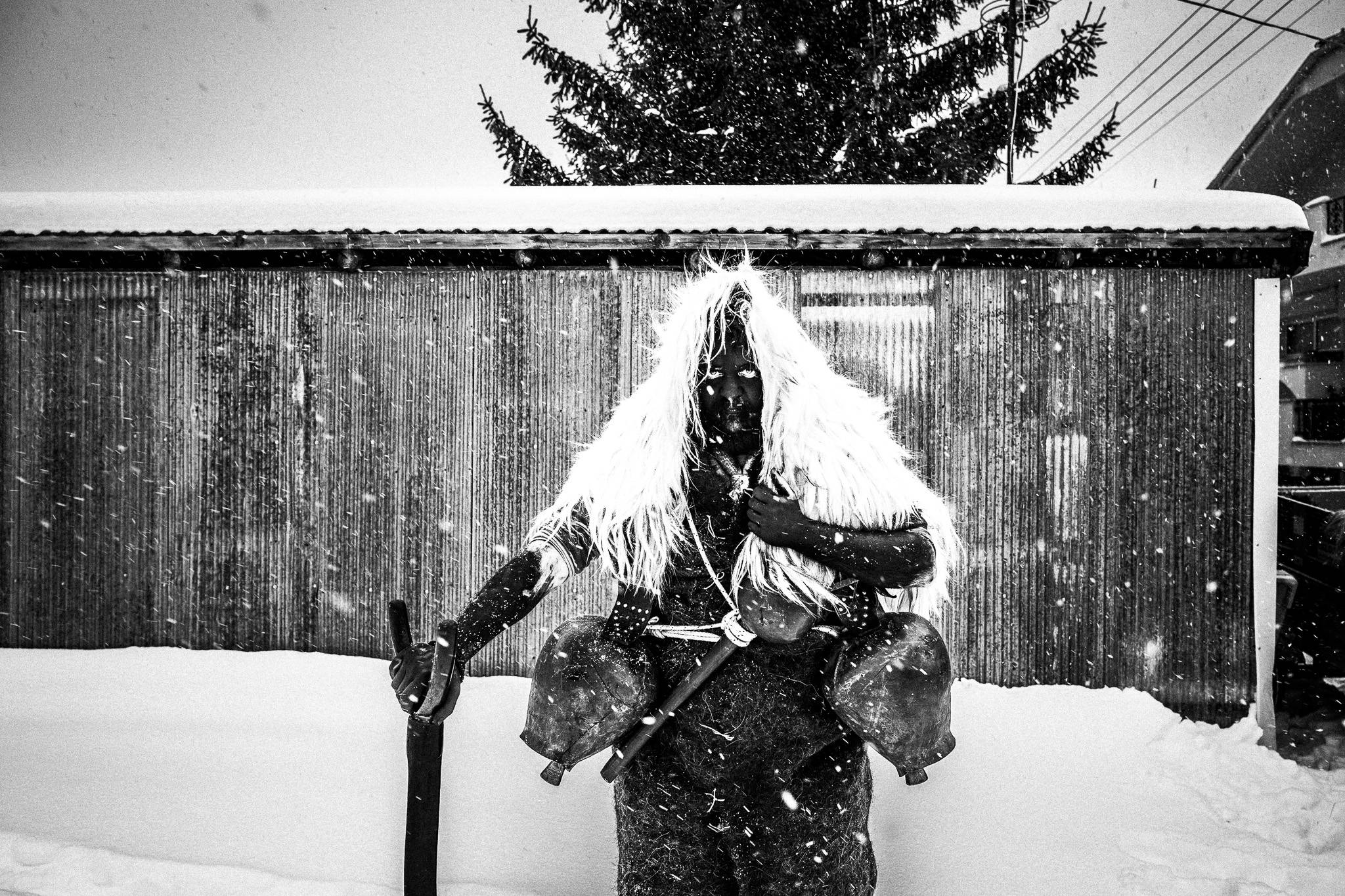 A bell-bearer during the custom of Arapides standing in front of a building in the snow at Volakas, Drama.