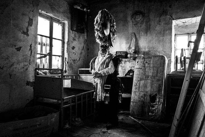 A masked bell bearer of Sohos standing inside an abandoned room.