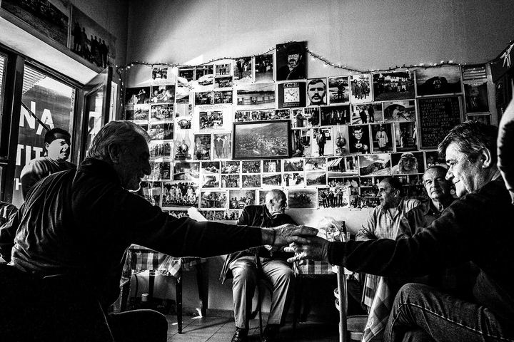 Black and white photograph of musicians playing brass instruments inside a crowded café in Florina.
