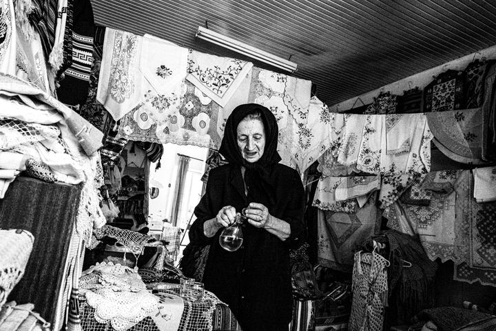 Black and white portrait of Hermione inside her textile shop in Anogia, surrounded by woven fabrics and traditional cloths.