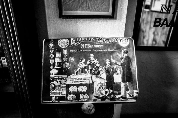 Black and white photograph of a vintage Kitron Naxou poster inside a distillery in Naxos.