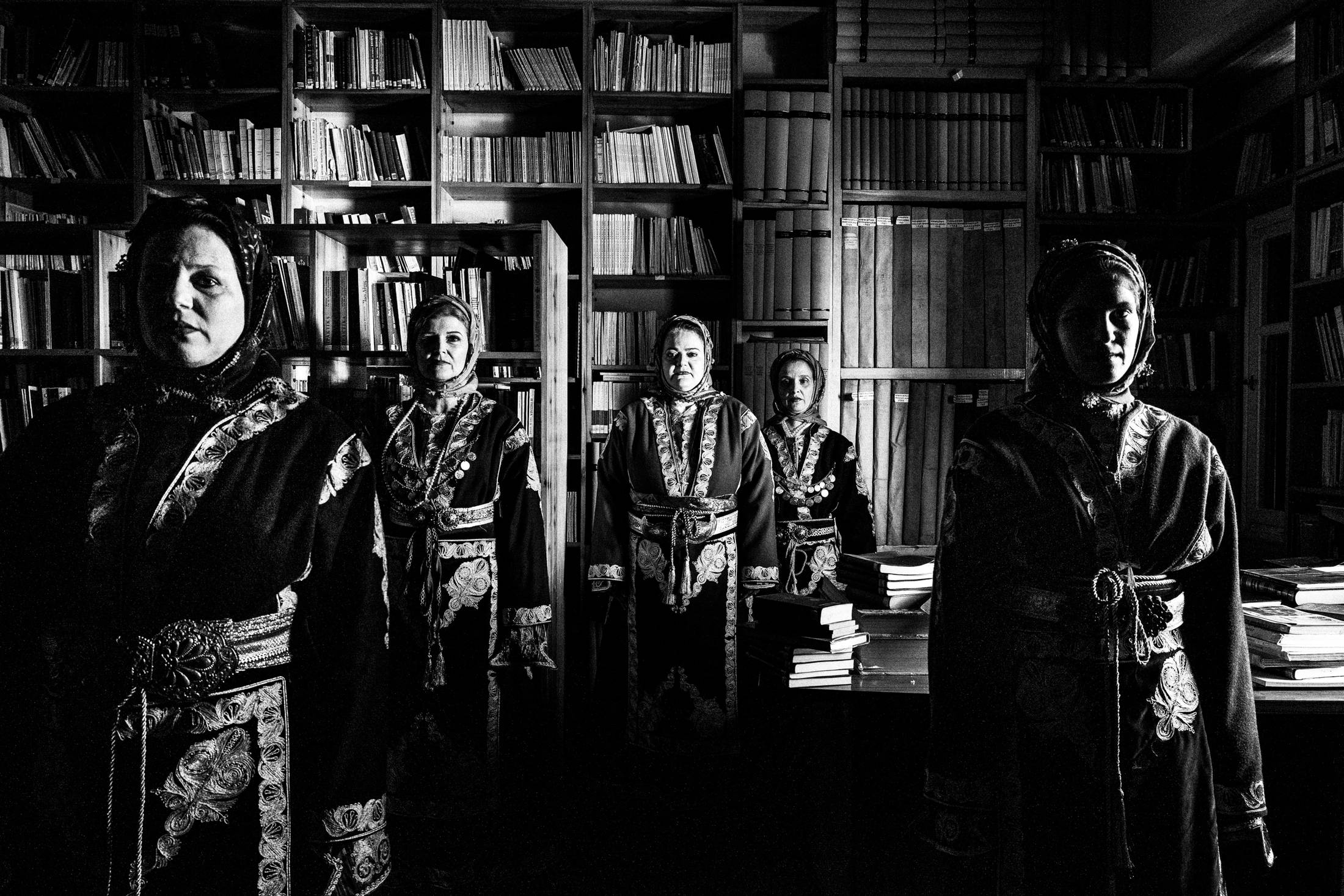 Five women standing in formation, wearing the costumes of Cappadocia, inside the library of Faros Varvassiou on the island of Chios