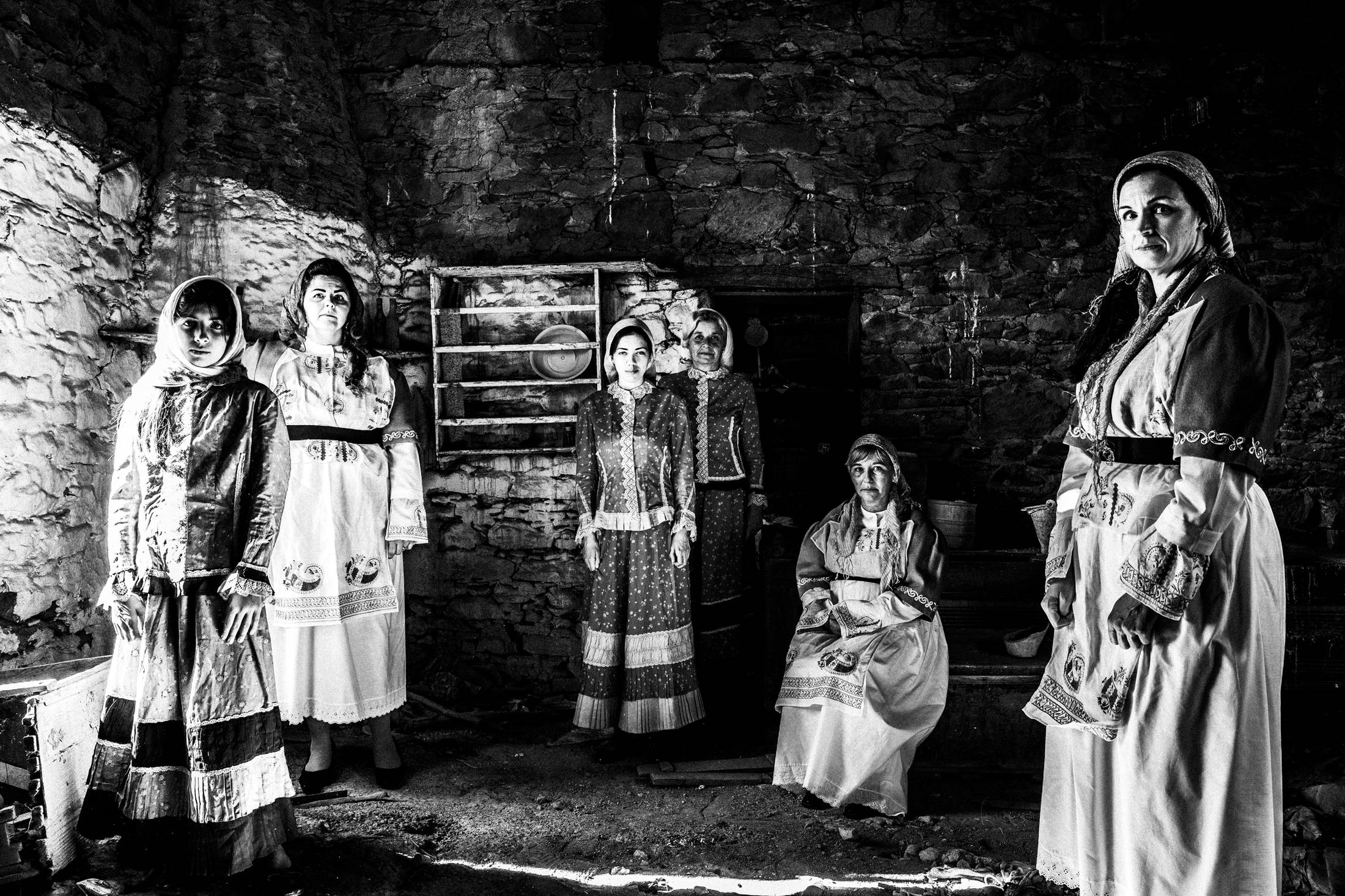 Five women inside the kitchen of an old abandoned local house, wearing the traditional costumes of Volissos, Chios
