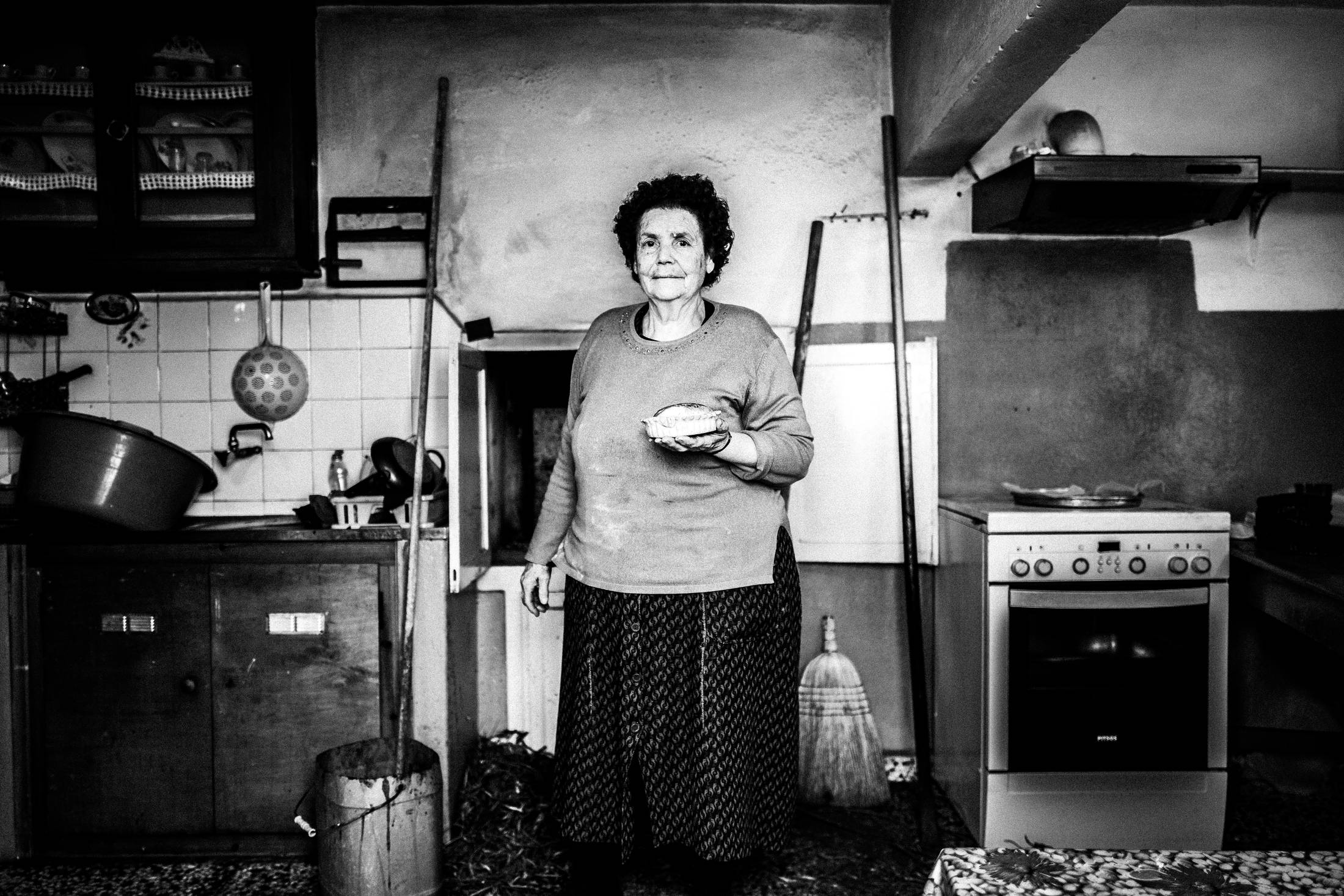 Black and white photograph of Moscha Gryllis holding a freshly baked Patiniotiki pie in a kitchen in Patmos.