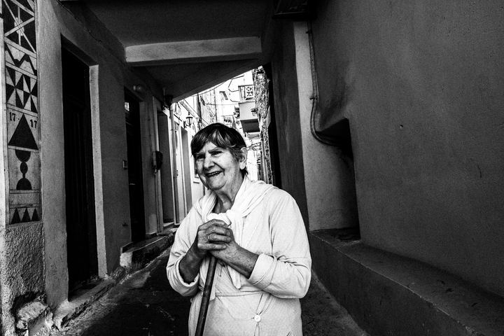 Black and white photograph of a woman in Pyrgi, Chios, with xysta patterns visible on the surrounding façades.