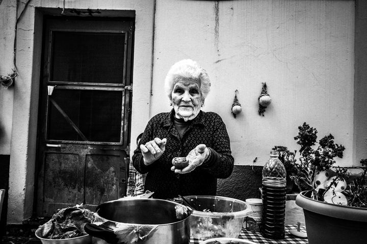 Black and white photograph of Chryssi preparing giaprakia outside her home in Patmos.