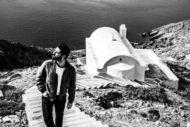 Black and white photograph of Yannis Philippakis near a white chapel above the sea in Olympos.