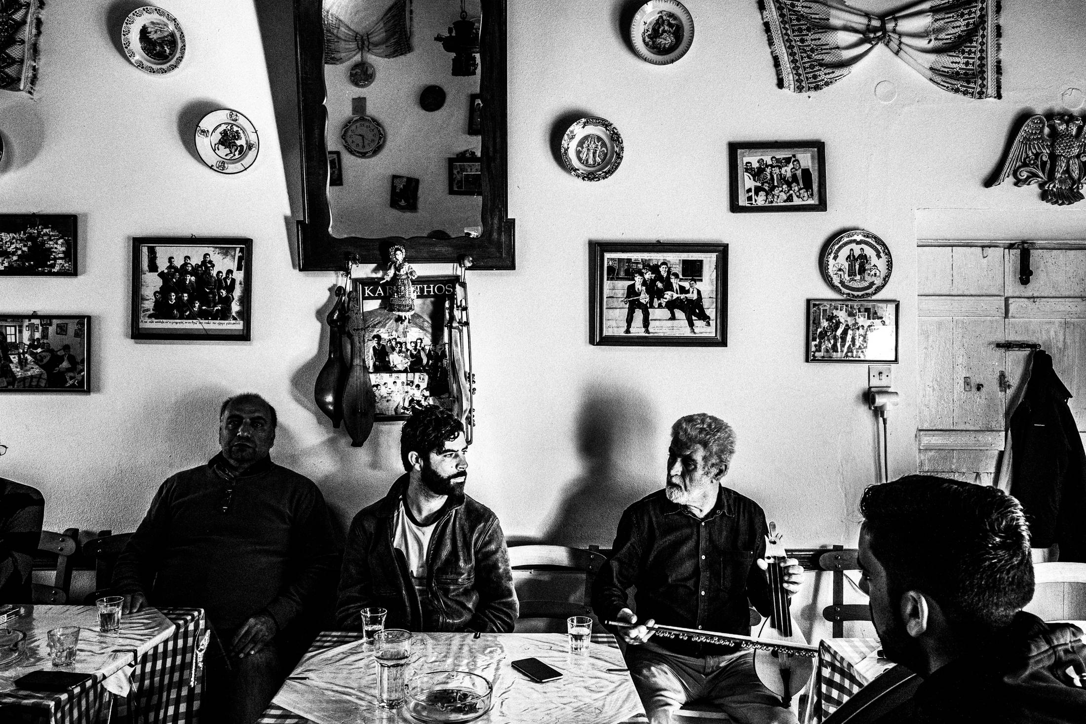 Black and white photograph of Yannis Philippakis sitting beside his father in a café in Olympos while music is played.
